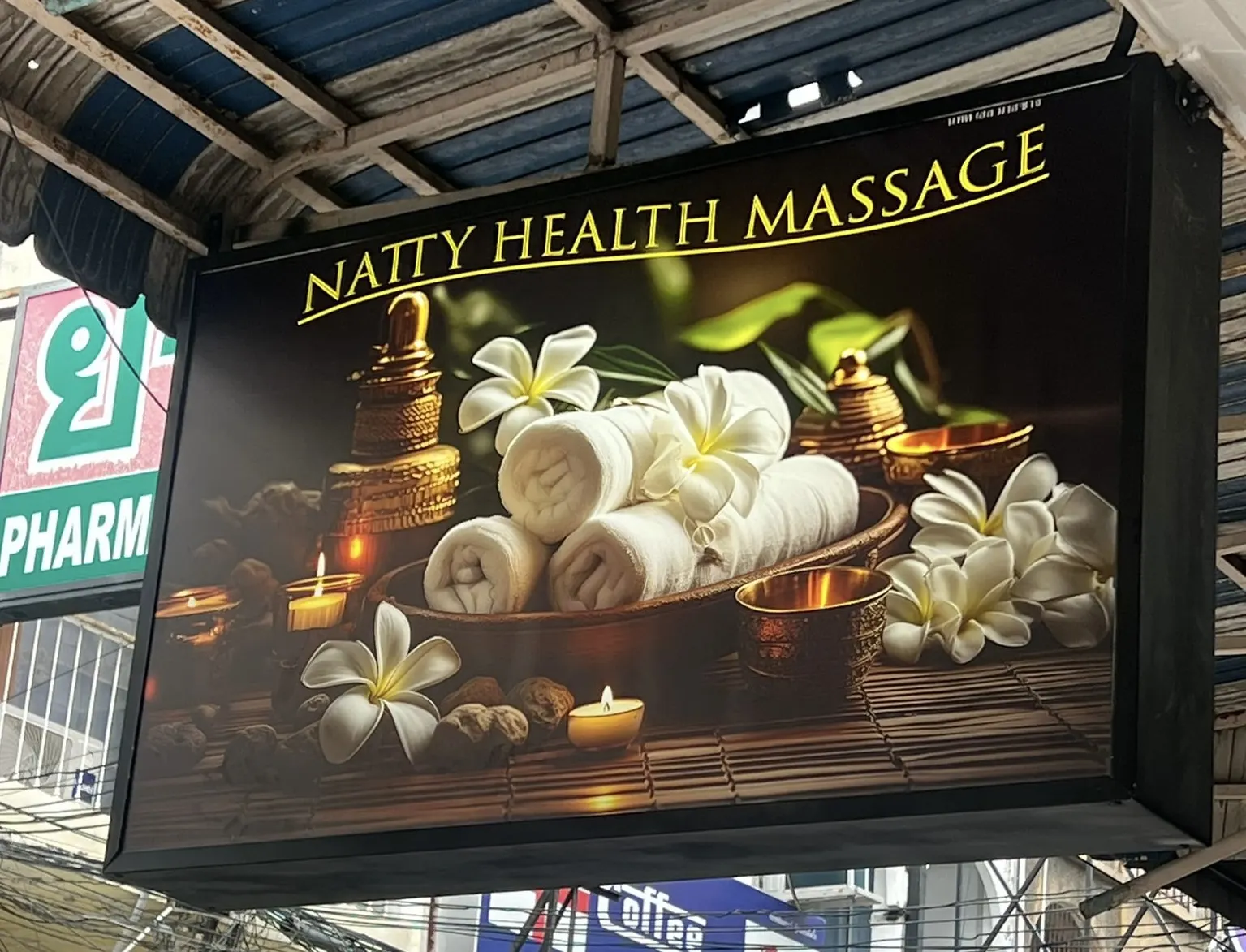 The illuminated Natty Health Massage sign: rolled white towels, plumeria flowers and candles